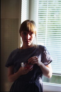 Portrait of young woman standing against window