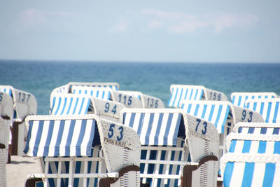 Hooded chairs on beach by sea against sky