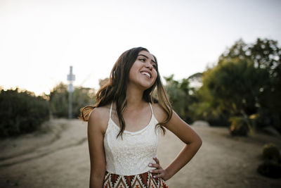 Happy teenage girl looking away while standing against clear sky in garden during quinceanera at sunset