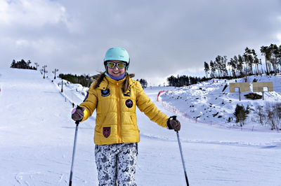 Happy young woman in yellow jacket and ski helmet on mountain slope, winter sports, alpine skiing 