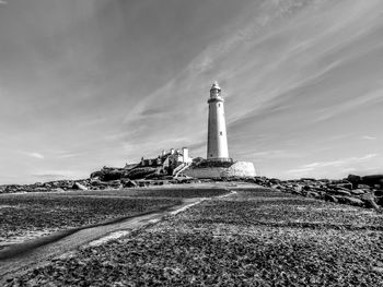 Lighthouse on field by building against sky