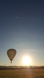 Hot air balloon flying over field against sky during sunset