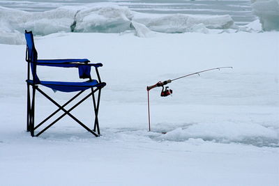 Empty foldable chair with fishing rod on snow