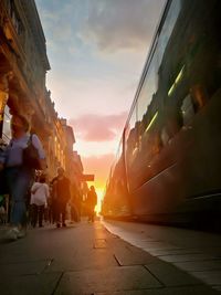 People on street in city against sky during sunset