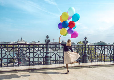 Woman with colorful balloons on walkway against sky in city