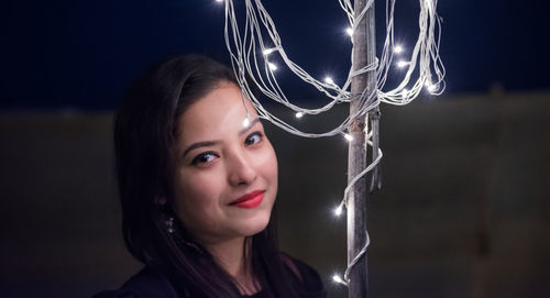 Close-up portrait of woman by illuminated string lights at night