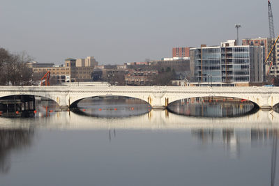 Bridge over river by buildings against sky