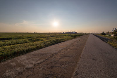 Road amidst field against sky during sunset