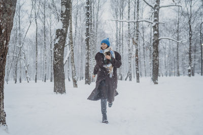 Smiling woman running near trees in snow at park