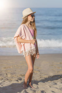 Portrait of a girl in a hat and black glasses in full growth on the background of the sea. 