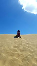 Low angle view of man kneeling on sand dune against blue sky
