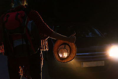 Back view of unrecognizable female hitchhiker standing on dark road and catching car at night during vacation