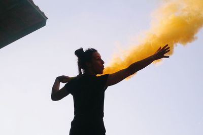Young woman holding distress flare against clear sky