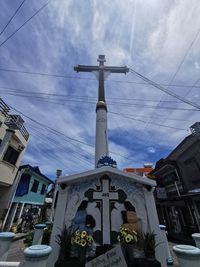 Low angle view of cross amidst buildings against sky