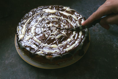 Cropped hand of person cutting chocolate cake on table