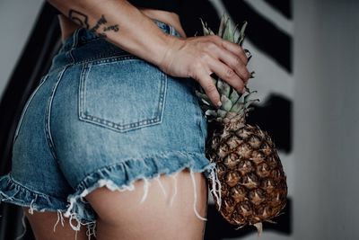 Midsection of woman wearing denim shorts holding pineapple