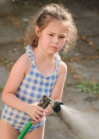 Cute gril in a bathing suit playing with water hose on a warm afternoon