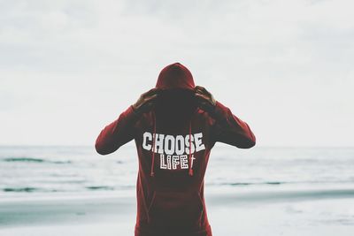 Man in hooded clothing standing against sea