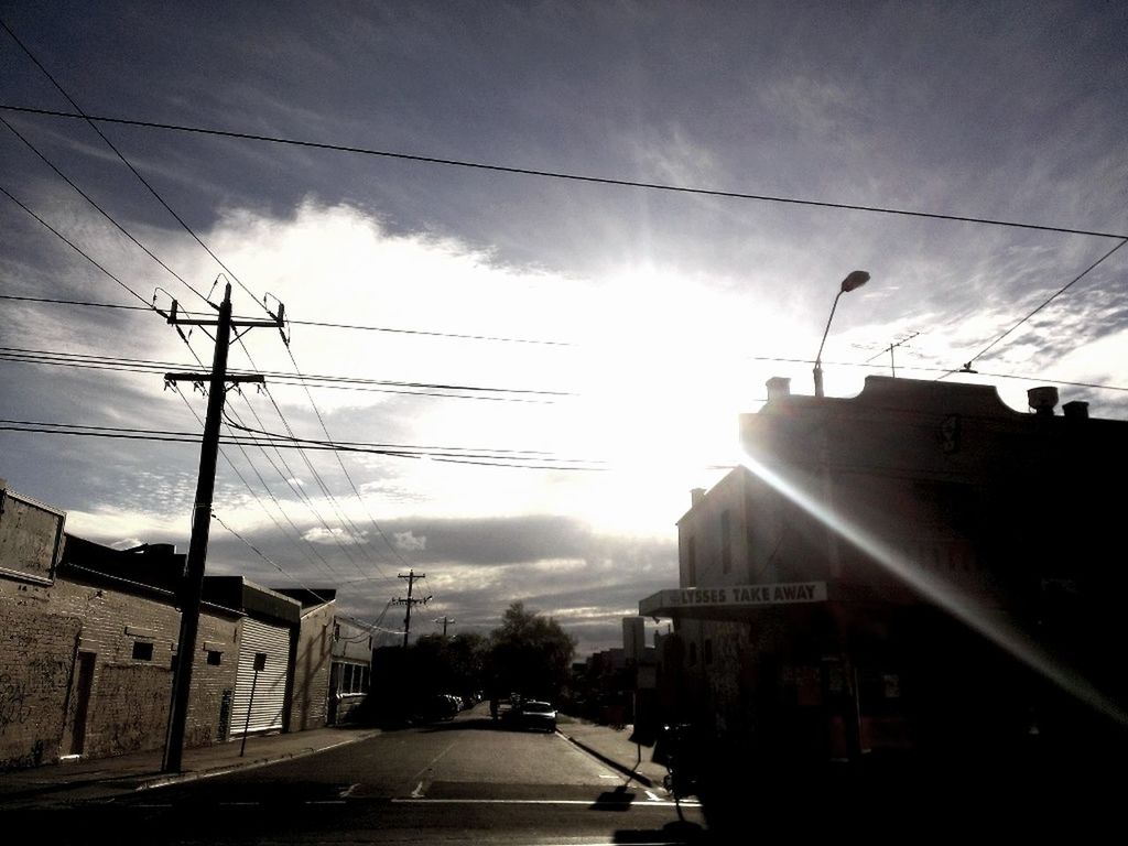 building exterior, transportation, built structure, power line, sky, architecture, electricity pylon, car, street, road, cable, sun, power supply, cloud - sky, electricity, sunlight, land vehicle, mode of transport, city, sunbeam