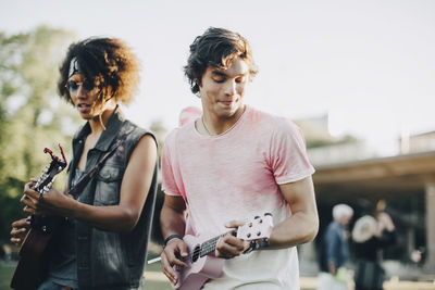 Happy young men playing ukulele at music concert in summer