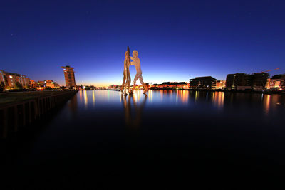 Illuminated buildings by river against clear sky at night