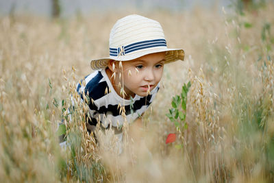 Cute little boy in a straw hat is sitting on an oat field playing hide and seek. funny kid hiding in