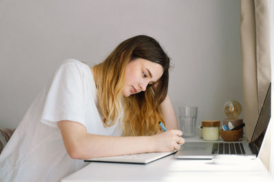 A teenage girl is drawing or doing homework in the bedroom. a teenager studies at home.