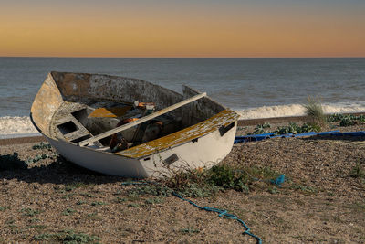 Abandoned boat moored on beach against sky during sunset
