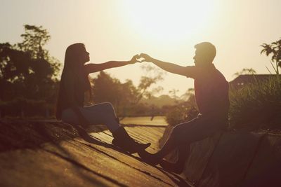 Midsection of couple sitting against sky during sunset