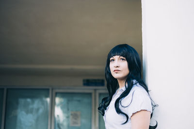 Woman looking away while standing against wall