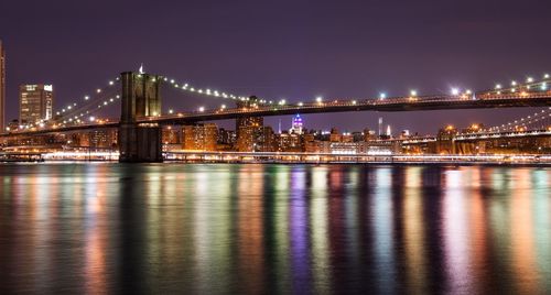 Brooklyn bridge over east river against sky in illuminated city at night