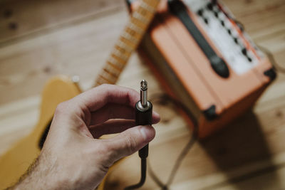 Cropped hand of person holding interconnect plug over guitar and equipment