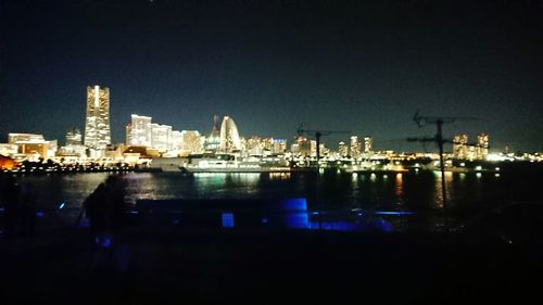 Illuminated city by river against sky at night