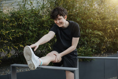 Young man looking away while sitting on railing against plants