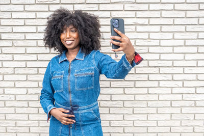Portrait of young woman using mobile phone against brick wall