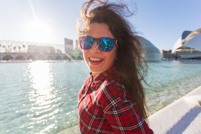 Portrait of young woman wearing sunglasses against lake