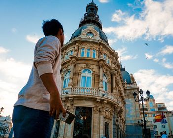 Low angle view of man standing by building against sky