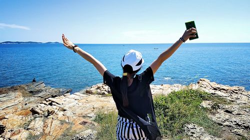 Woman with arms raised looking at sea while standing on cliff