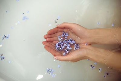 Woman is lying in the bath with water in the spa and holds small blue forget-me-nots in her hands