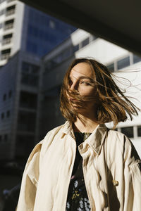 A woman in a raincoat walks around the city with her hair flying in th