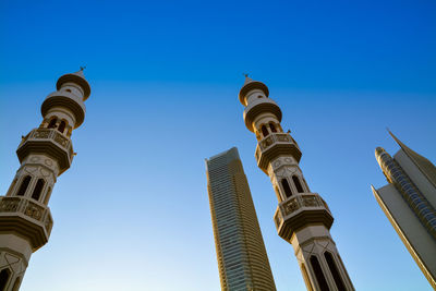 Low angle view of minarets and skyscrapers against clear blue sky