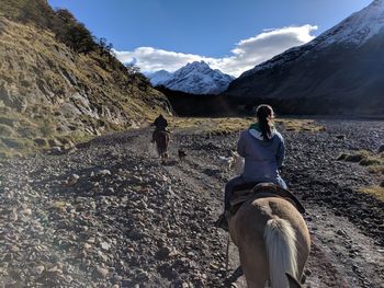 Rear view of people riding on mountain against sky