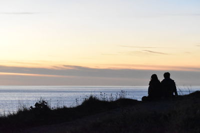 Silhouette couple looking at sea against sky during sunset