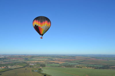 Hot air balloon flying over landscape against clear blue sky