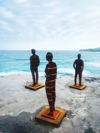 Metallic statues at beach against sky