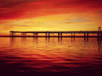 Silhouette pier by river against orange sky