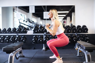 A woman squatting with a dumbbell in the gym.