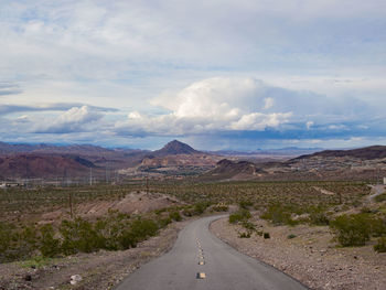 Country road along landscape and mountains against sky