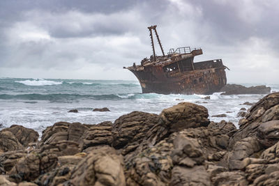 Shipwreck in sea against cloudy sky