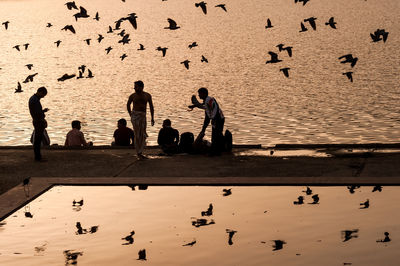 People on sea shore against sky during sunset